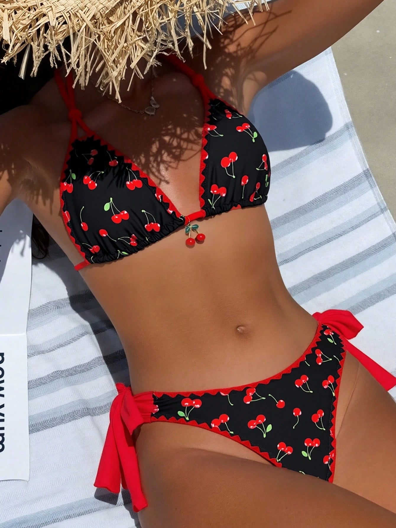 Person wearing a black bikini with red cherries pattern on a towel.