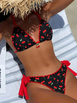 Person wearing a black bikini with red cherries pattern on a towel.