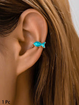 Close-up of an ear wearing a turquoise fish-shaped earring with blurred background