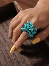 Hand wearing a turquoise ring with yellow nail polish on a wooden surface