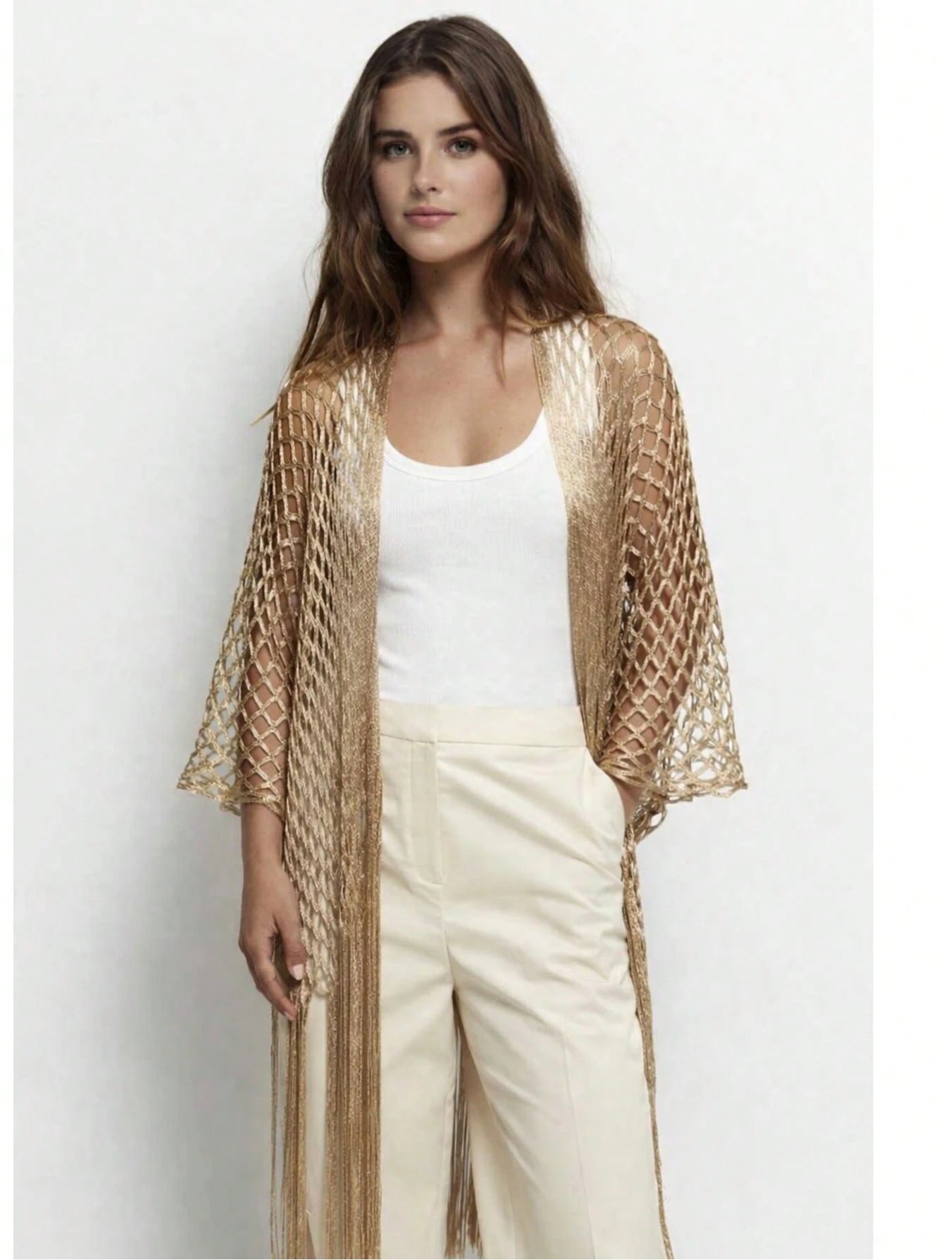 Woman wearing a beige mesh kimono over a white top and pants on a light gray background