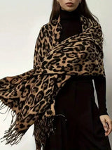 A woman wearing a large leopard-print shawl over a black turtleneck and black skirt, shown from the lips down against a plain light background.