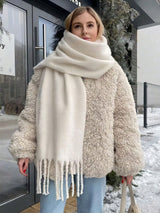 A woman wearing a chunky cream-colored teddy coat and a matching oversized cream scarf with fringe, standing outdoors in a snowy setting.