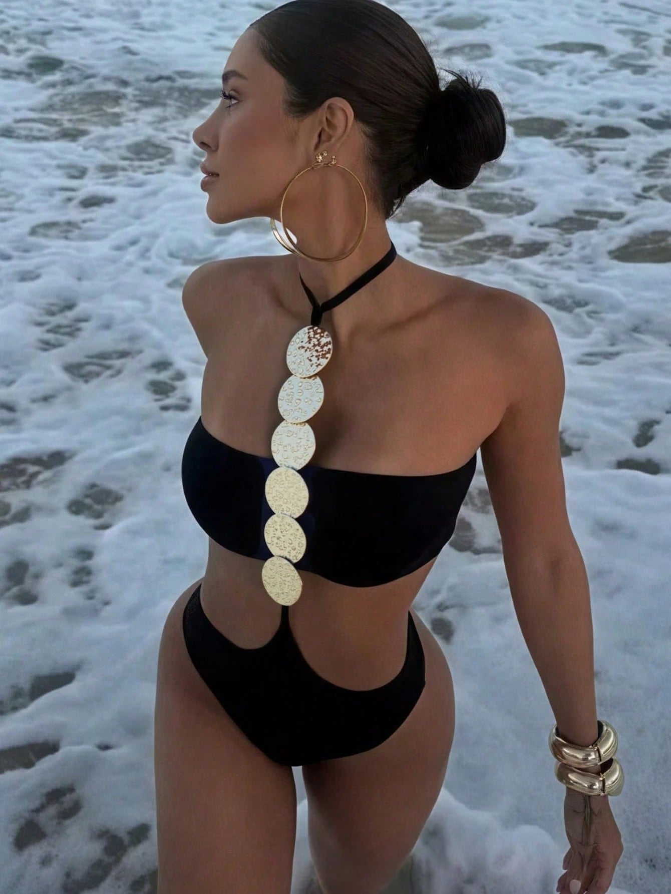 Woman in a black bikini with a decorative back piece on a beach.