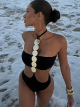 Woman in a black bikini with a decorative back piece on a beach.