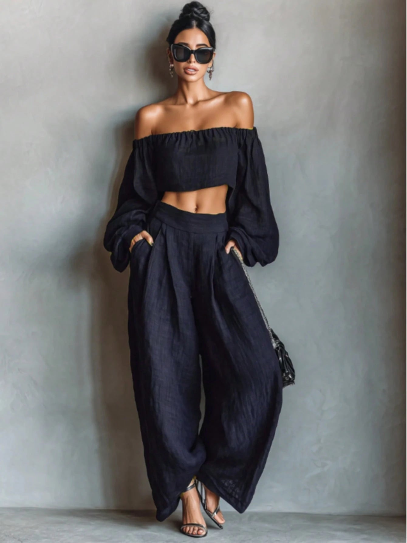 Woman wearing a black off-shoulder top and wide-leg pants against a gray background