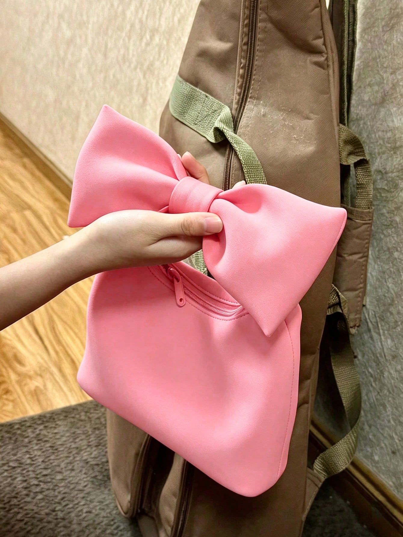 Pink bow-shaped object held by a hand against a brown bag.