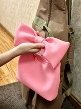 Pink bow-shaped object held by a hand against a brown bag.