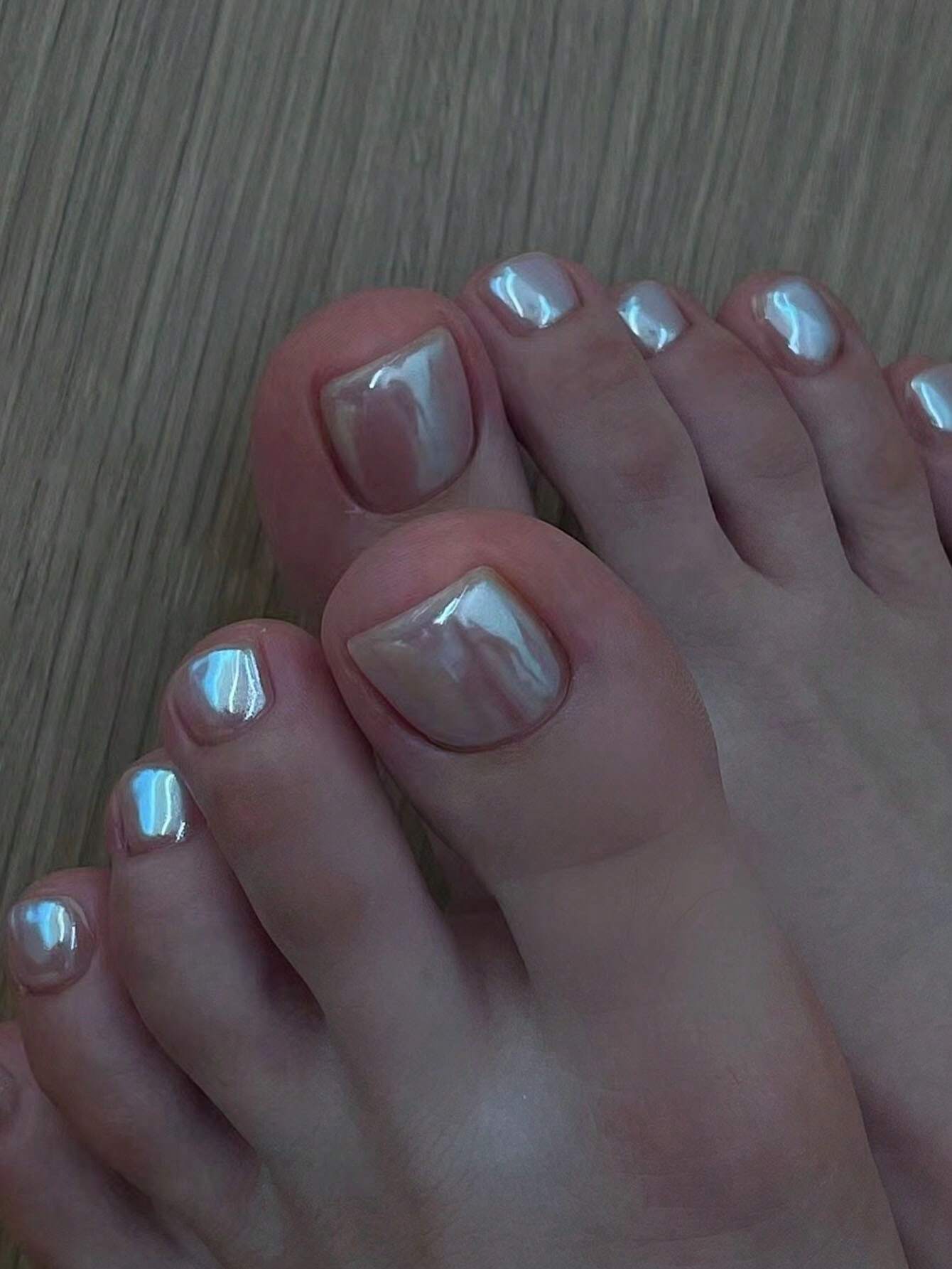 Close-up of feet with polished toenails on a wooden floor.