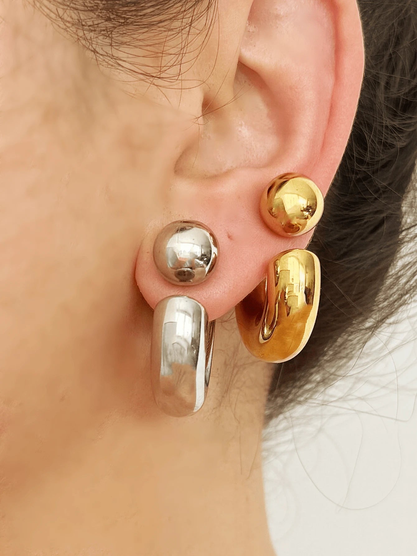 Close-up of an ear wearing gold and silver hoop earrings.