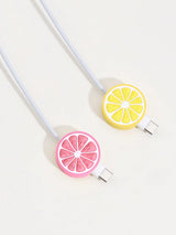 Two silicone cable protectors shaped like citrus slices, one pink grapefruit and one yellow lemon, attached to white cables on a light off-white background.