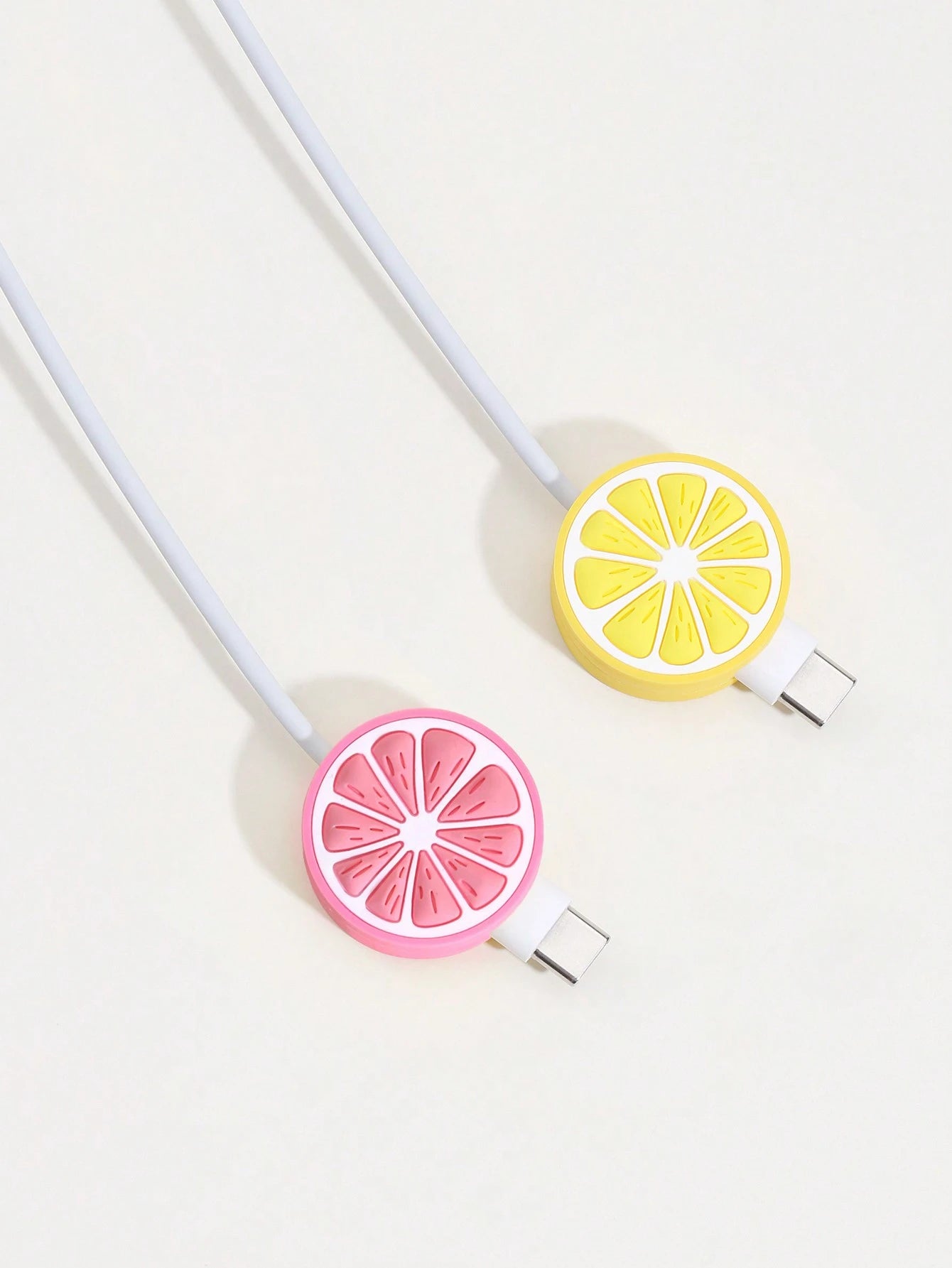Two silicone cable protectors shaped like citrus slices, one pink grapefruit and one yellow lemon, attached to white cables on a light off-white background.