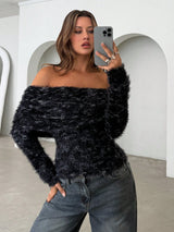 A woman takes a mirror selfie wearing a black and gray fuzzy off-the-shoulder long-sleeve sweater and dark gray jeans in a minimalist white room with arched walls.