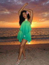 Woman in a green dress with a flower in her hair on a beach at sunset.
