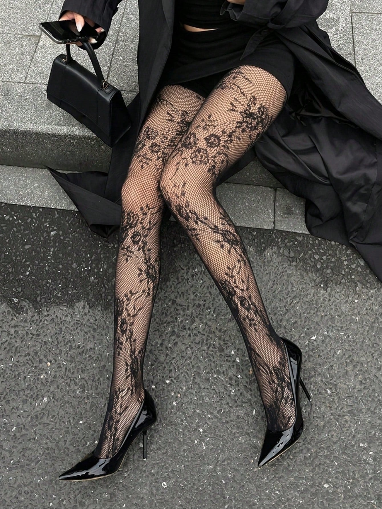 Person wearing black floral lace stockings and high heels on a city street.