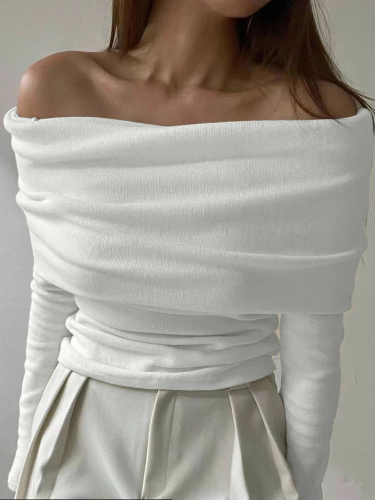White off-shoulder top worn by a person against a plain background