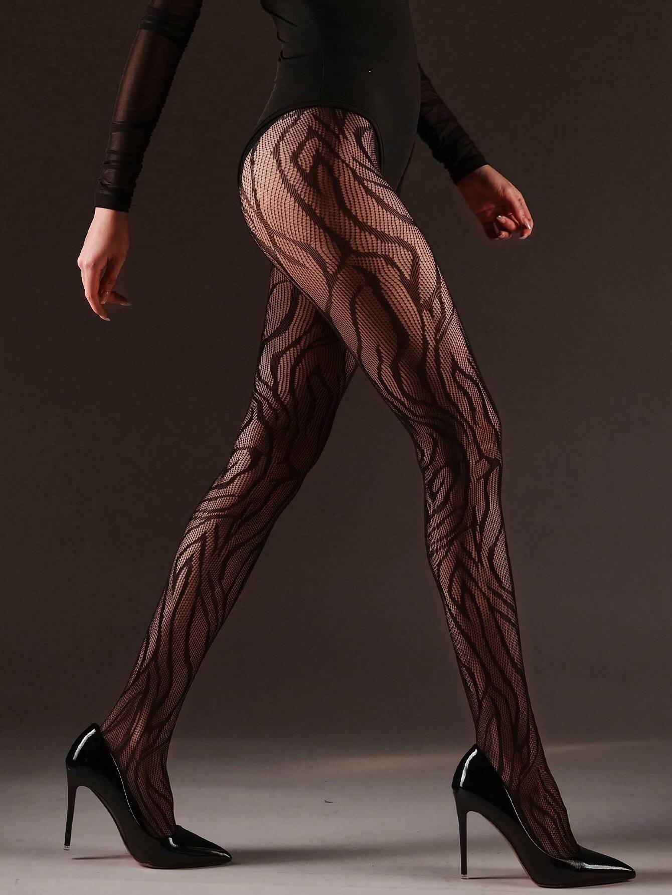 A model wearing sheer black patterned tights with a wavy abstract design, paired with a black bodysuit and black high heels, shown from the waist down against a dark gray studio background.