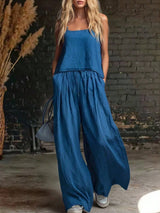Woman wearing a blue jumpsuit standing against a brick wall.
