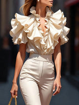 Woman wearing a beige ruffled blouse and pants with a blurred background