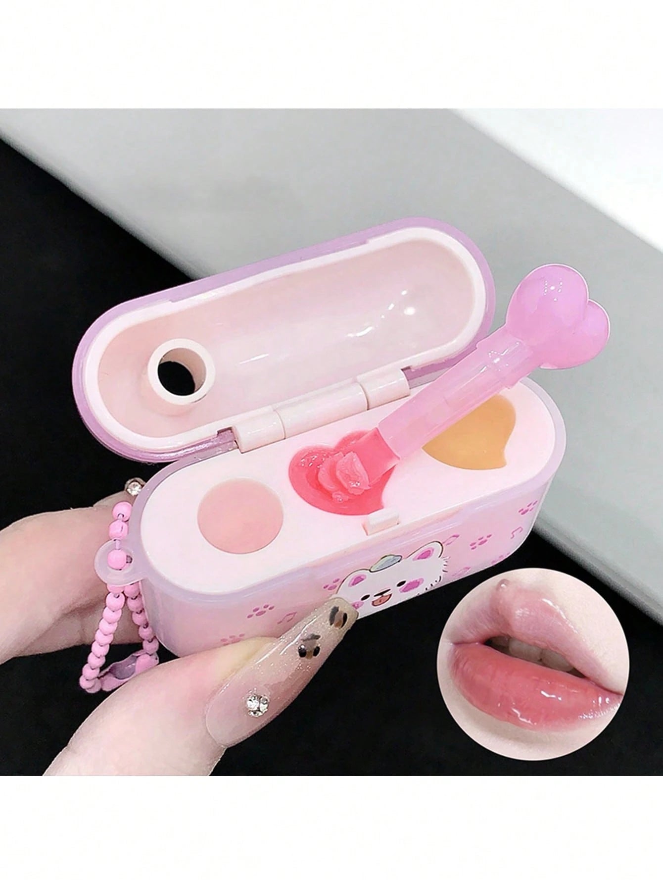 Pink lip gloss case with applicator and mirror, held by a hand.