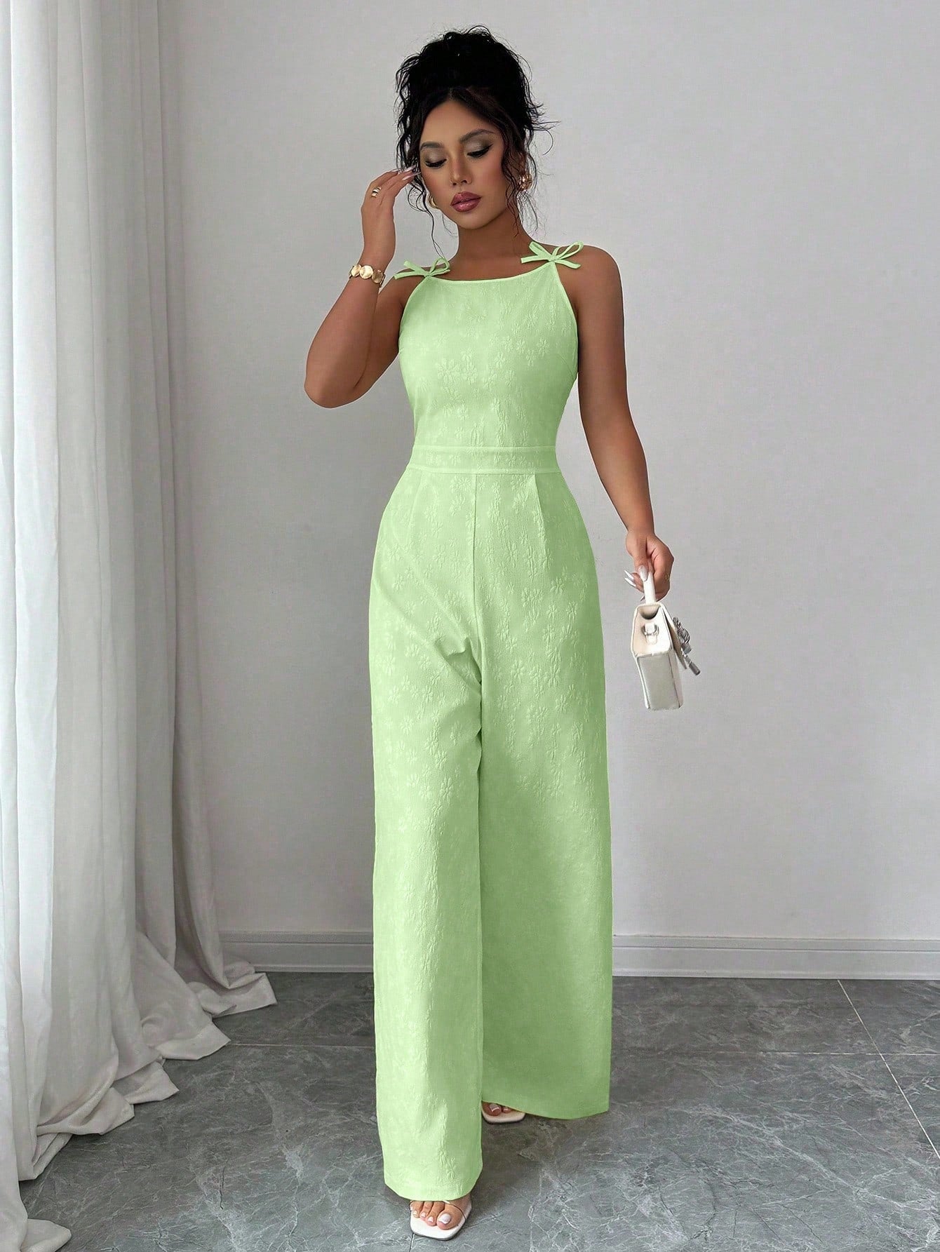 Woman wearing a light green jumpsuit standing against a plain background