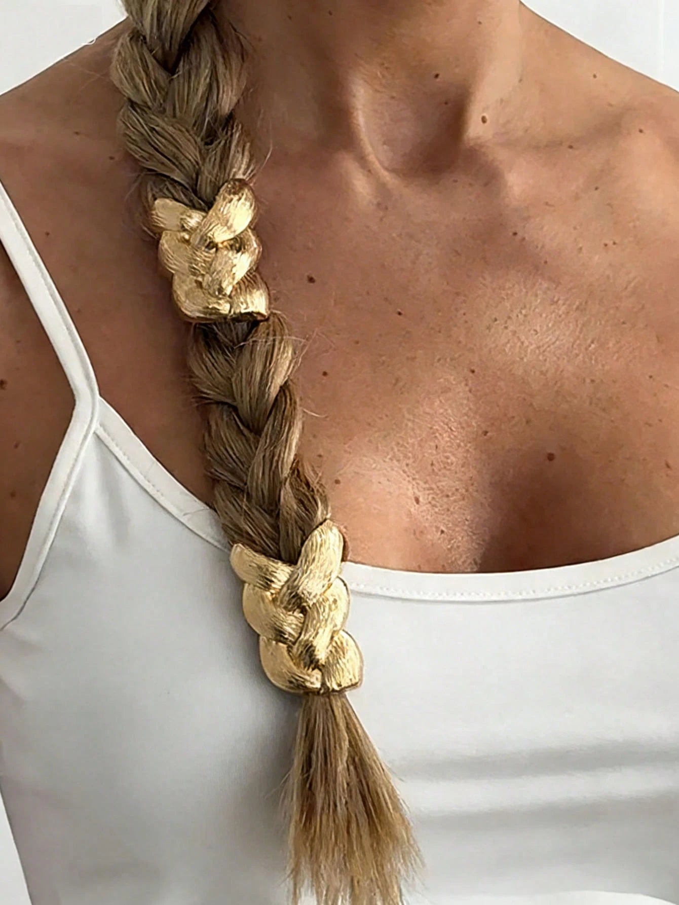 Person with braided hair adorned with gold hair accessories against a white background