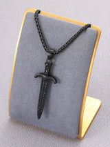 A black metal dagger pendant necklace displayed on a gray velvet jewelry bust with a gold-colored frame, set against a neutral gray background.