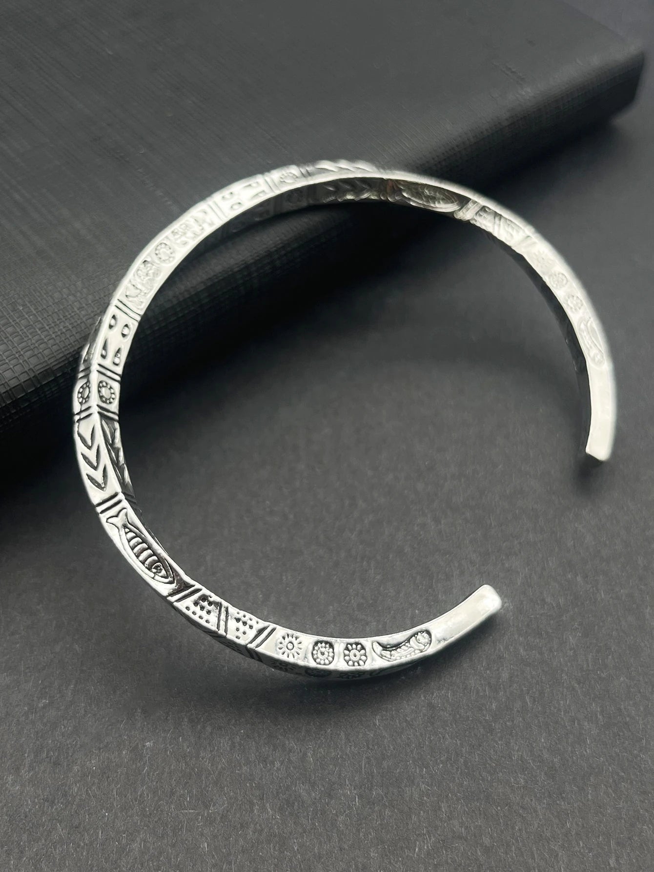 Silver bracelet with intricate patterns on a dark gray surface