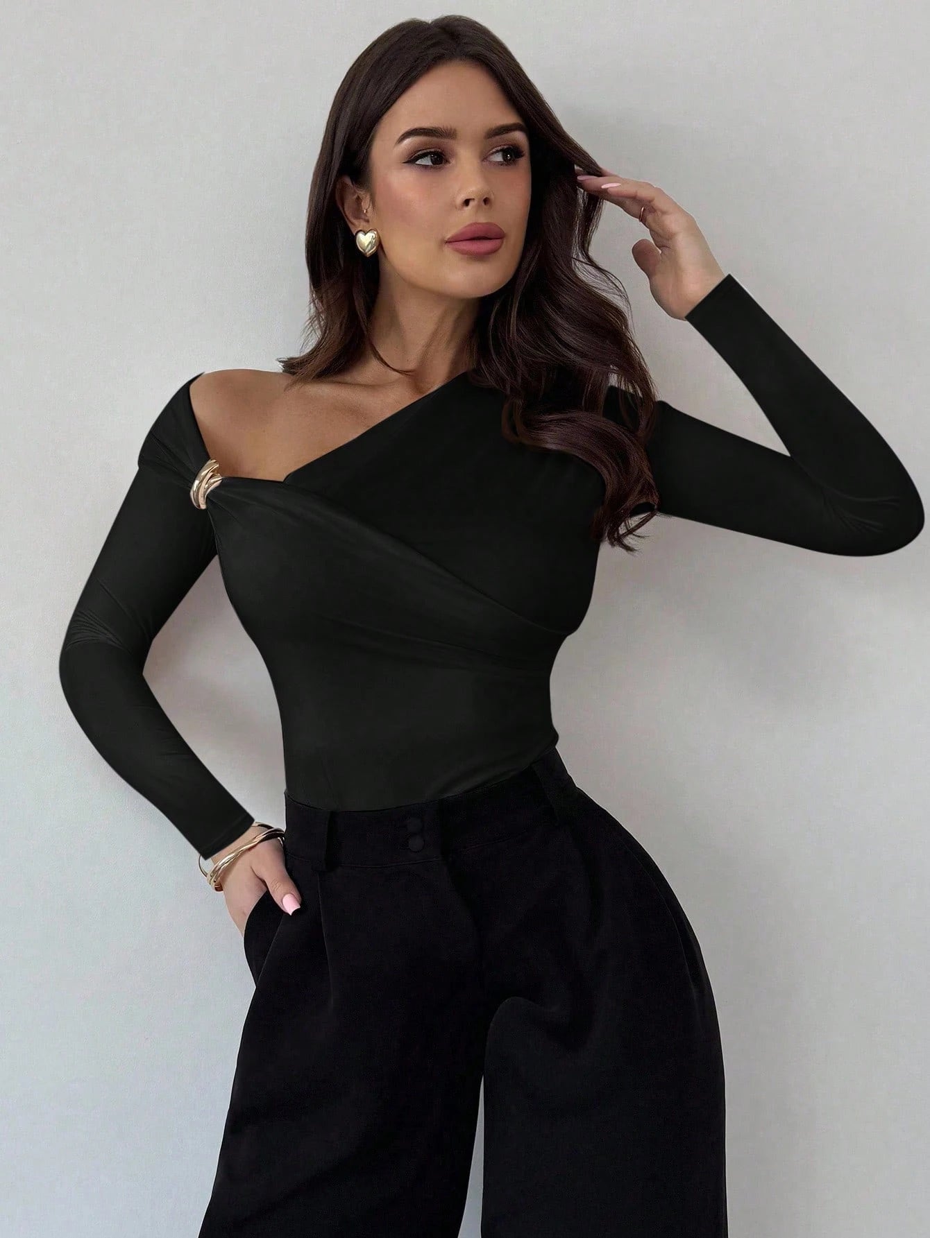 Woman wearing a brown one-shoulder top and black pants against a plain background