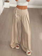 Person wearing beige wide-leg pants and a white top on a wooden floor.