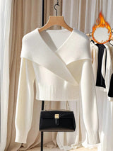 White sweater on a hanger with a black handbag below, against a neutral background.