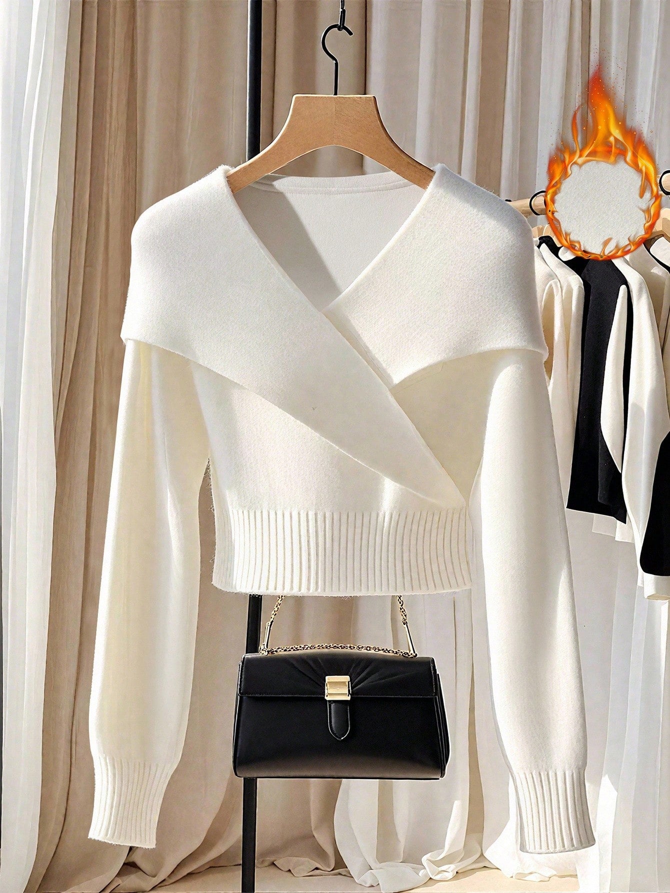 White sweater on a hanger with a black handbag below, against a neutral background.