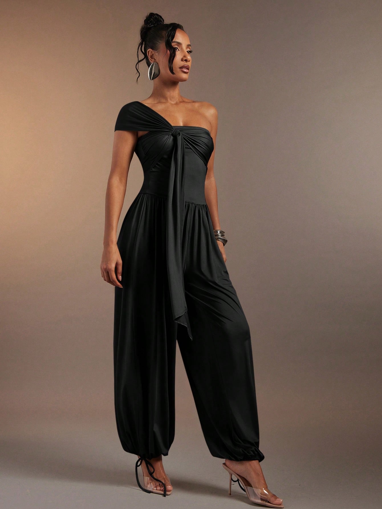 Woman wearing a black off-shoulder jumpsuit against a neutral background