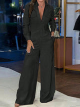 A woman wearing a dark charcoal gray wide-leg jumpsuit with a button-up front and chest pockets, standing in a boutique setting.