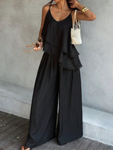 Woman wearing a black layered outfit with wide-leg pants against a gray wall.