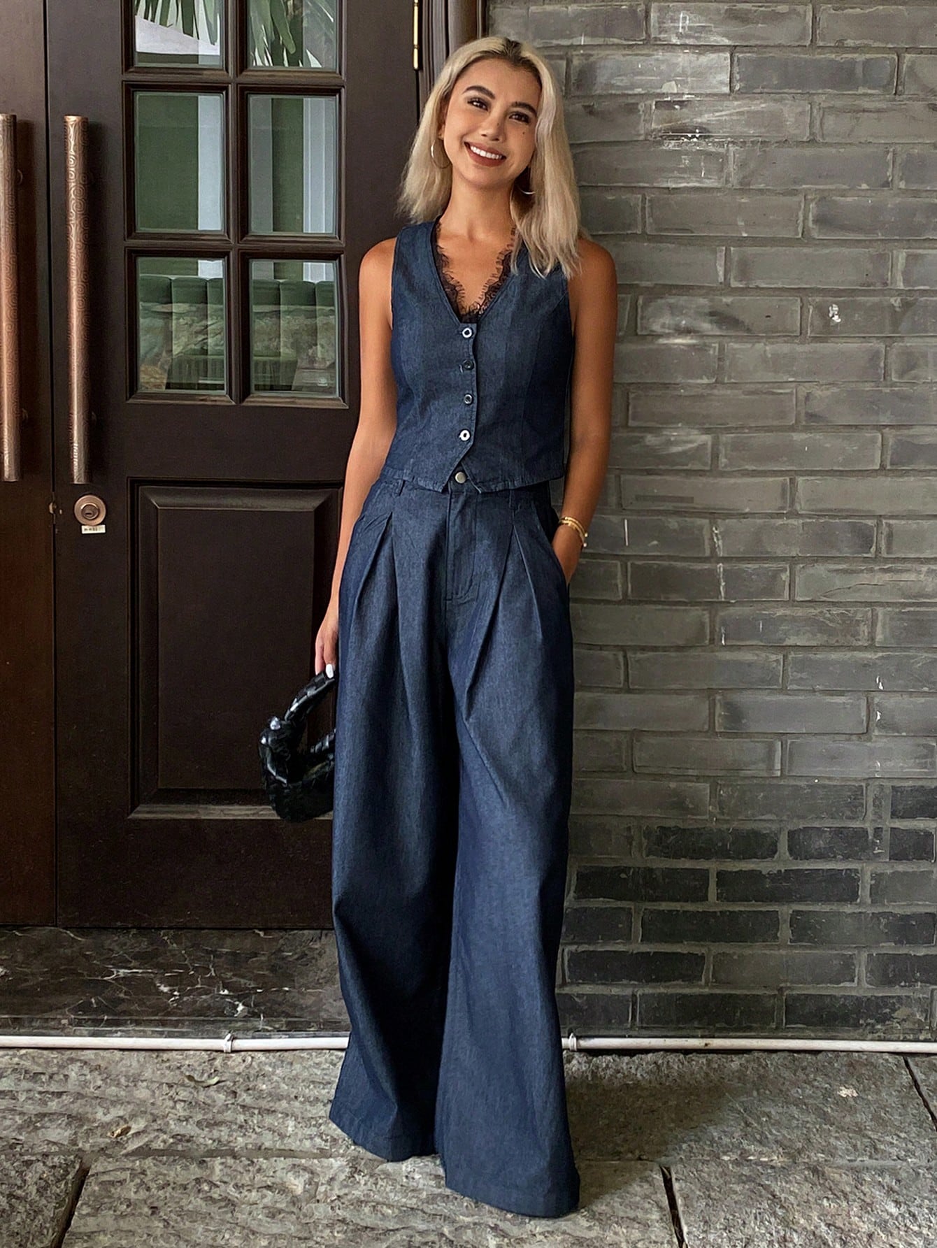 Woman wearing a blue denim jumpsuit standing against a brick wall.