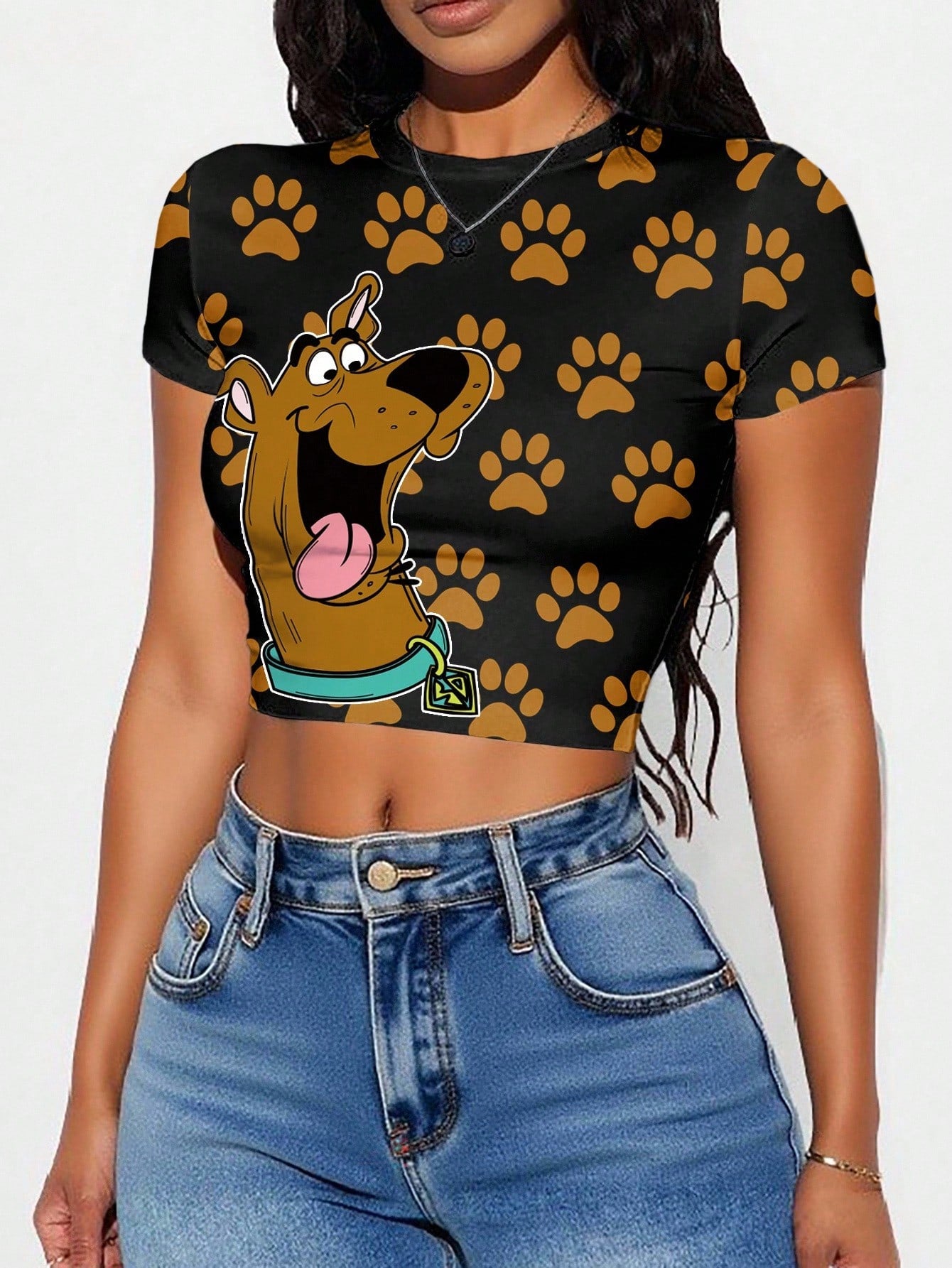 Person wearing a black crop top with cartoon character and paw prints, paired with blue jeans.