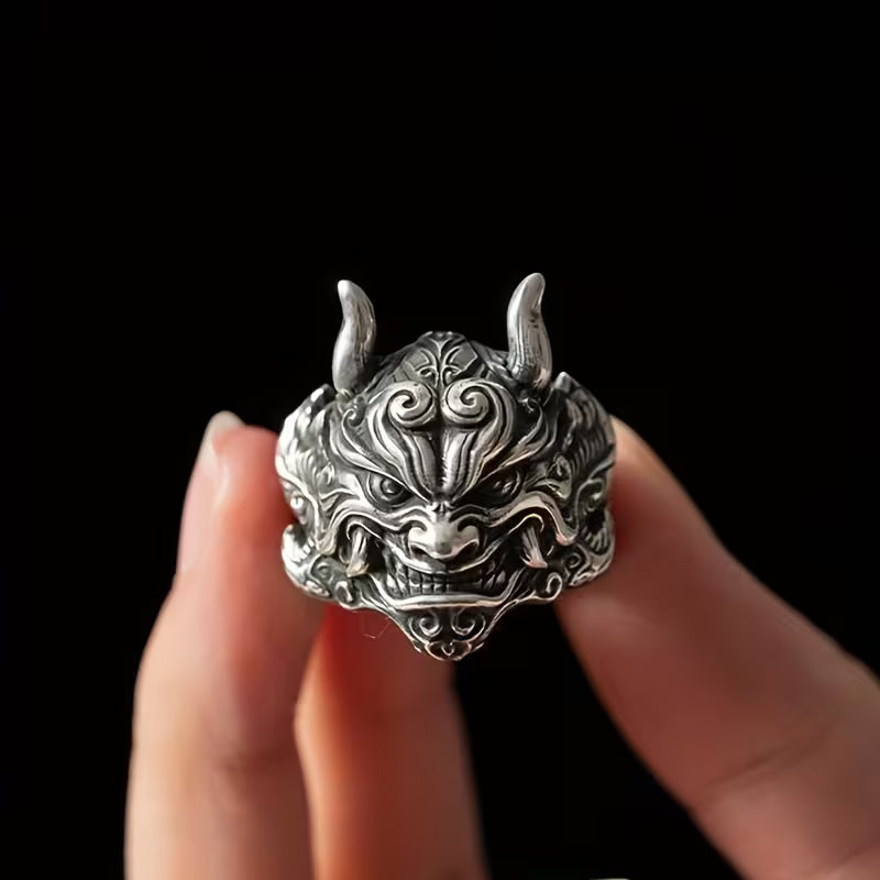 Silver dragon head ring held between fingers against a black background
