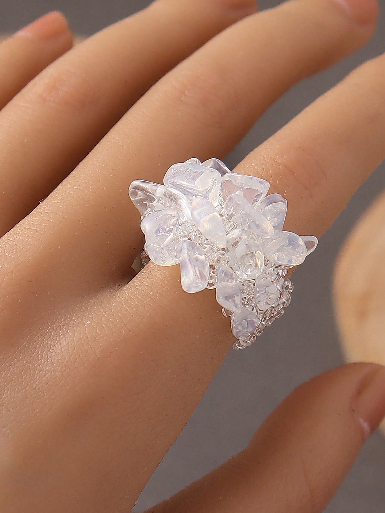 Close-up of a hand wearing a floral silver ring with clear stones on a neutral background