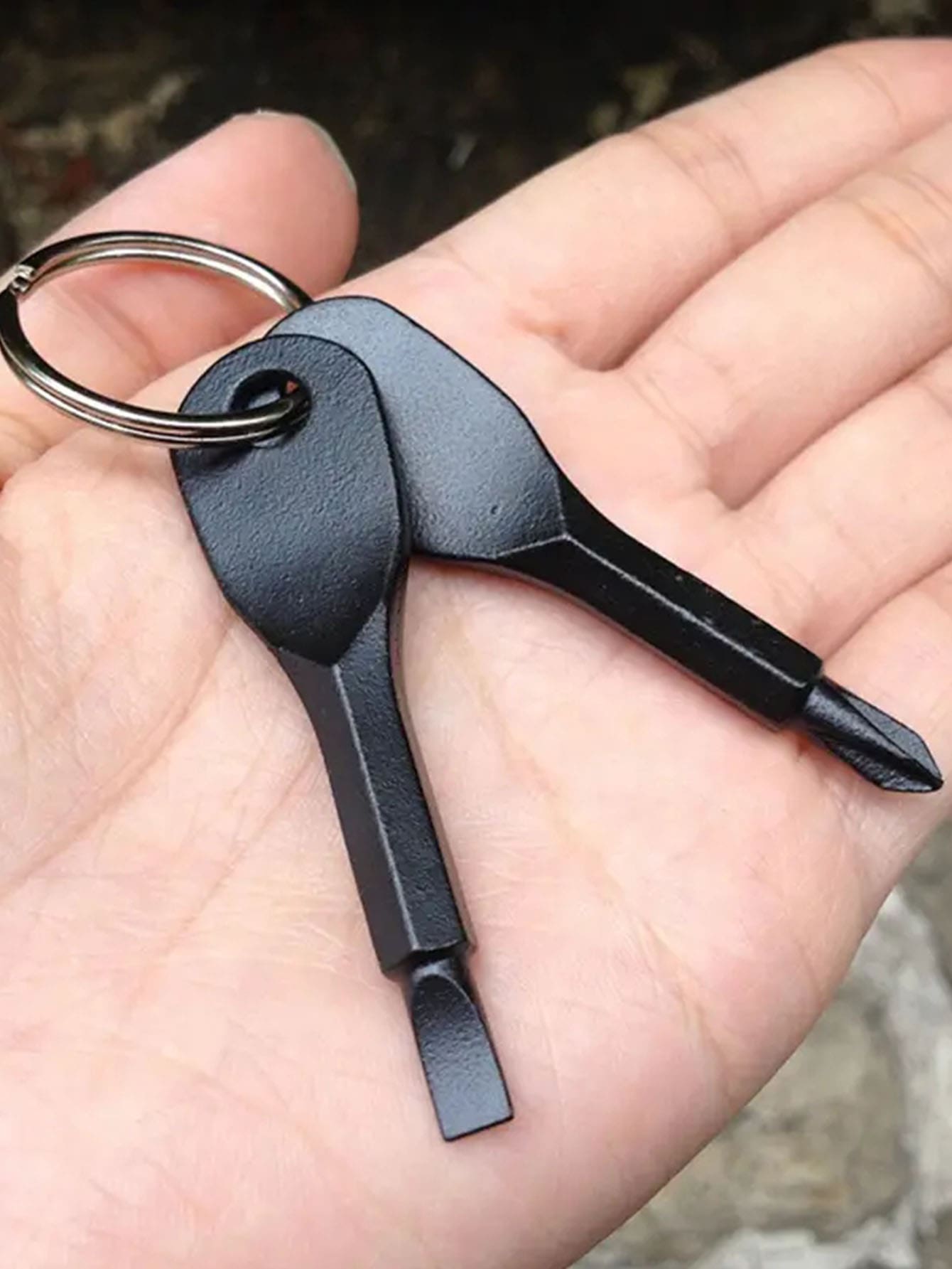 Multi-tool keychain with a keyring held in a hand against a blurred natural background