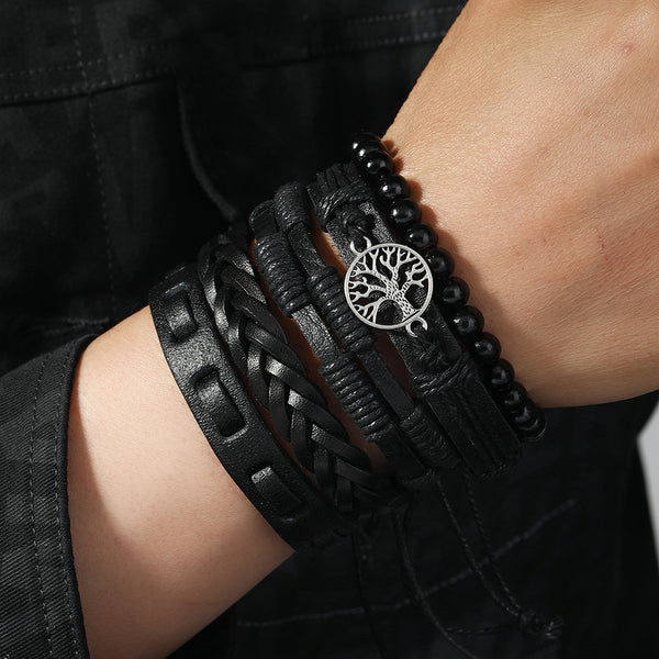 Close-up of a wrist wearing multiple black bracelets with a silver tree-of-life charm.