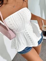 A woman wearing a white strapless eyelet peplum top with blue denim shorts, carrying a light pink shoulder bag and holding an iced coffee.