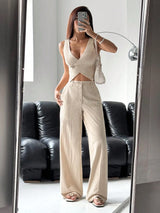 Woman taking a mirror selfie wearing a beige sleeveless top and wide-leg pants.