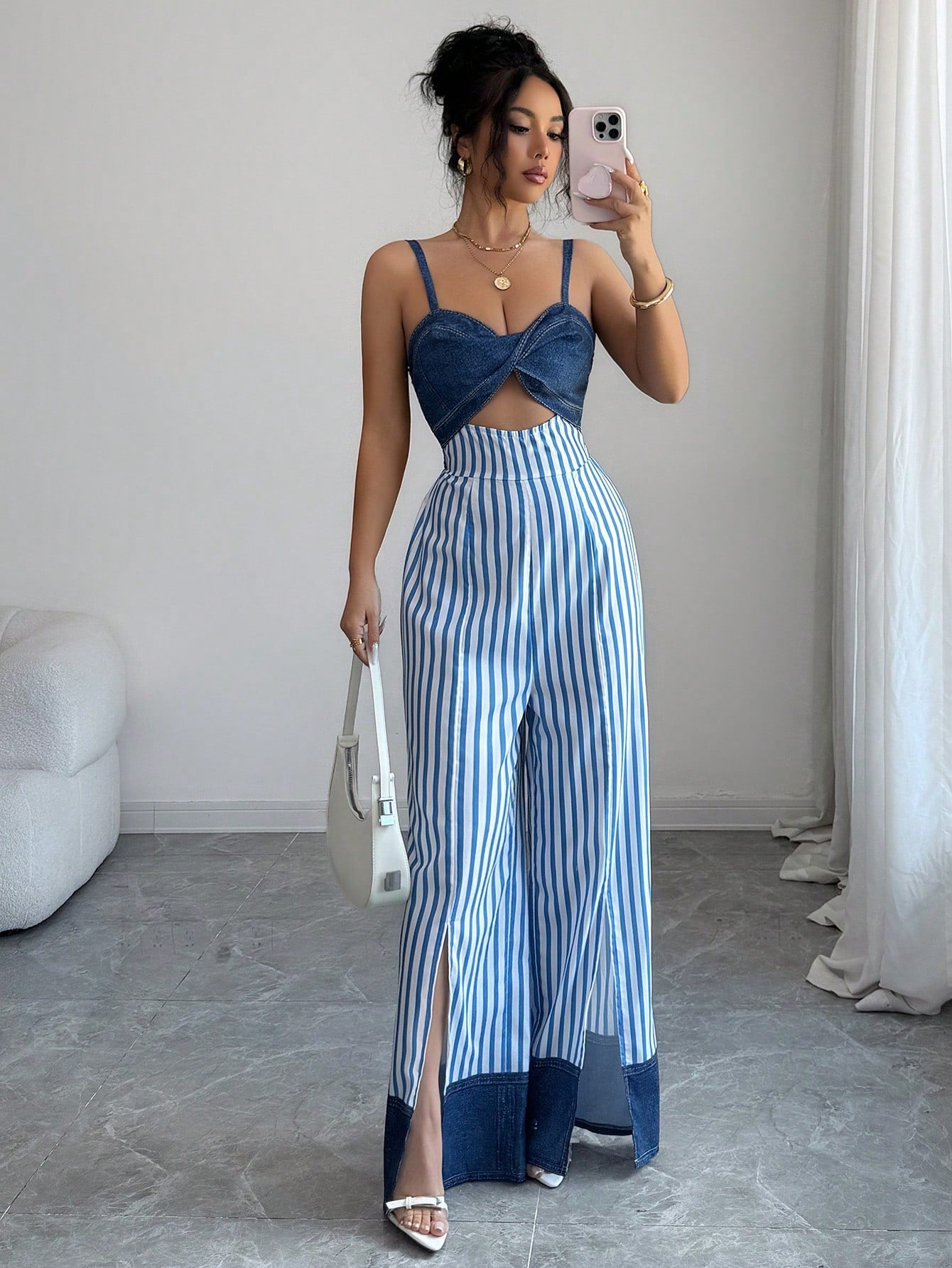 Woman taking a mirror selfie wearing a blue top and striped pants in a minimalistic room.