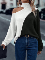 Person wearing a black and white sweater with blue jeans on a blurred street background