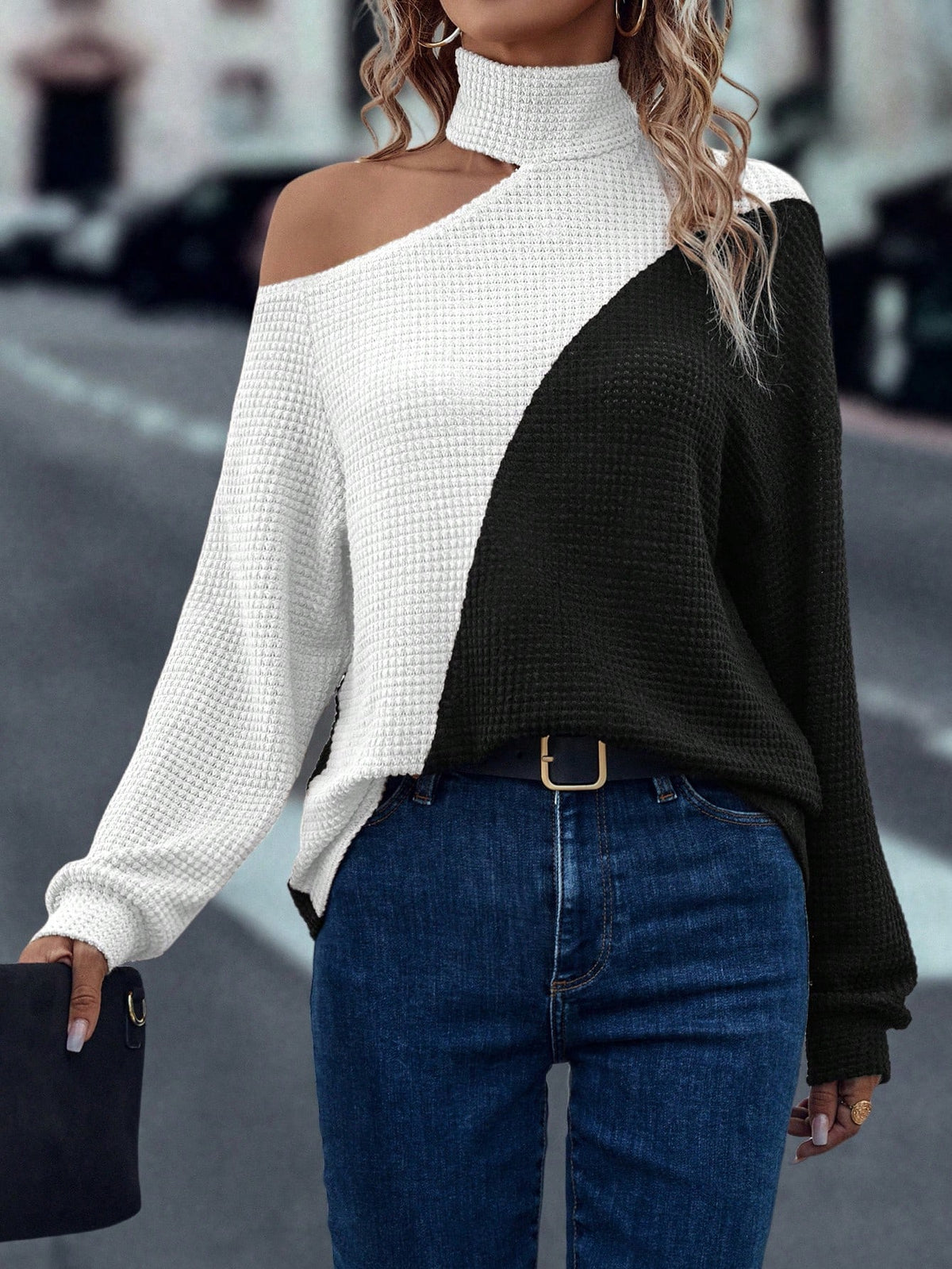 Person wearing a black and white sweater with blue jeans on a blurred street background