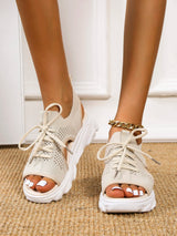 Beige open-toe shoes worn indoors on a neutral background