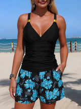 Woman wearing a black tank top and blue floral shorts on a beach.