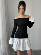A woman modeling a black off-the-shoulder long-sleeve mini dress with contrasting white bell sleeves and a white skirt, standing indoors against a light gray wall and curtain.
