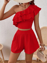 Person wearing a red ruffled top and shorts set against a white wall.